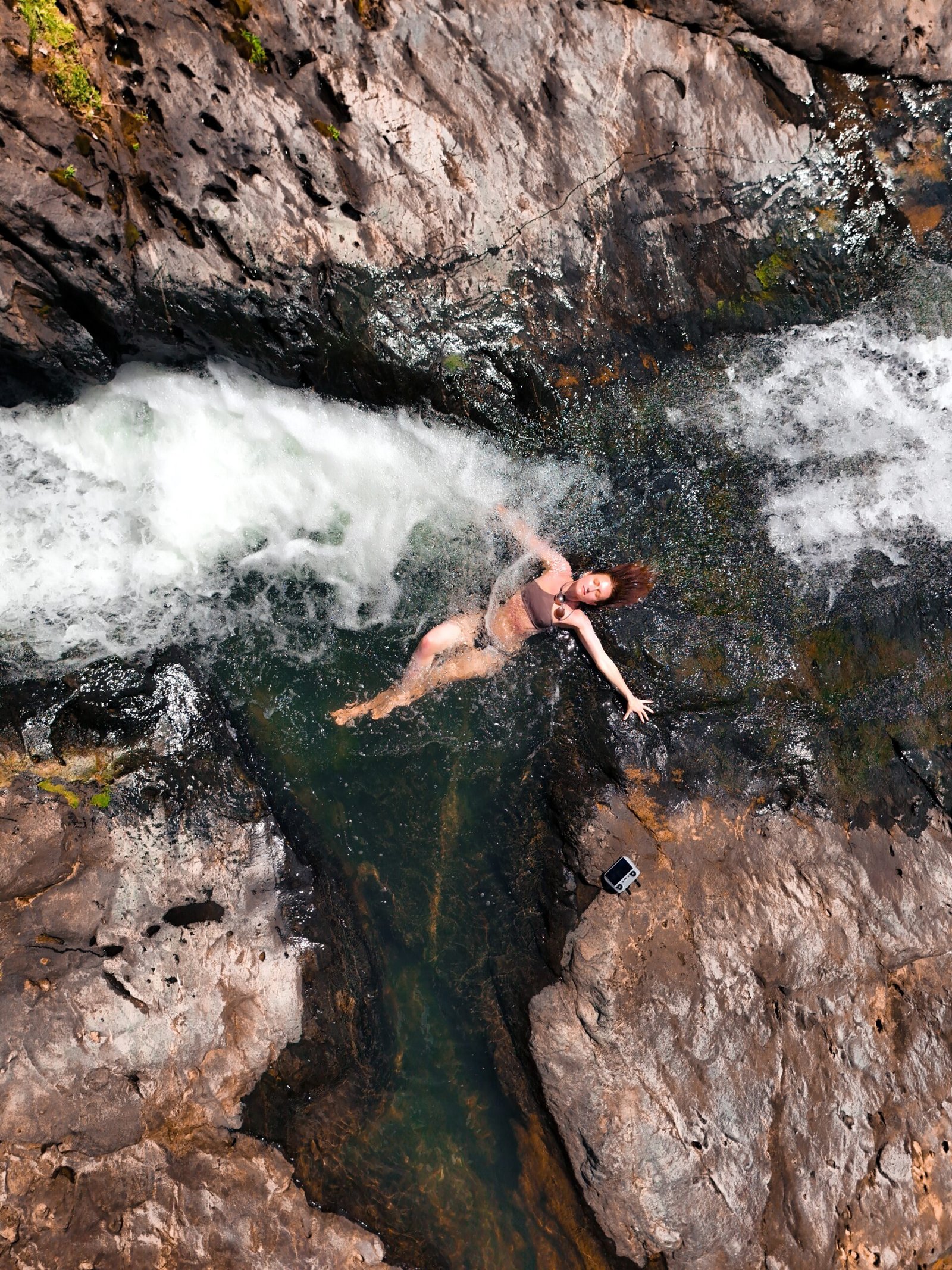 A drone shot of a woman laying in a waterfall in the El Yunque Jungle in Puerto Rico
