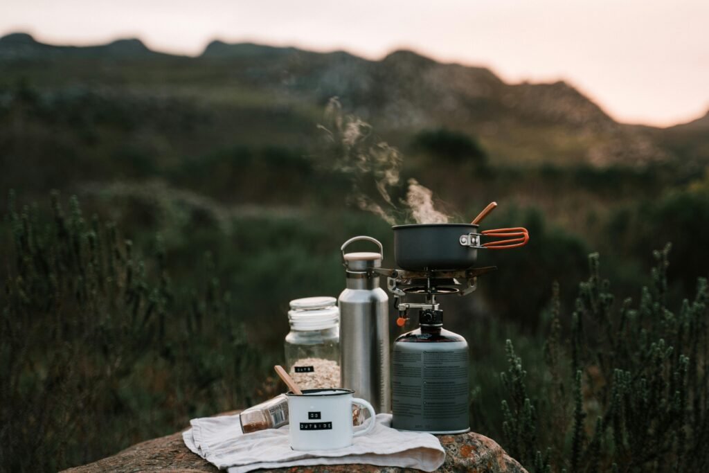 Outdoor camping cooking setup with stove, pot, and mug on a rock in nature.