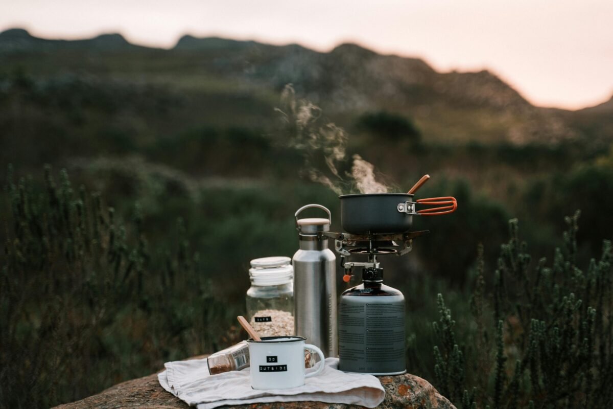 Outdoor camping cooking setup with stove, pot, and mug on a rock in nature.