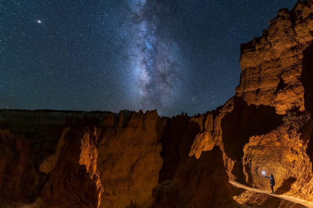 pexels-photo-6021541-6021541 A lone traveler explores Bryce Canyon at night, illuminated by the Milky Way in a clear starry sky.